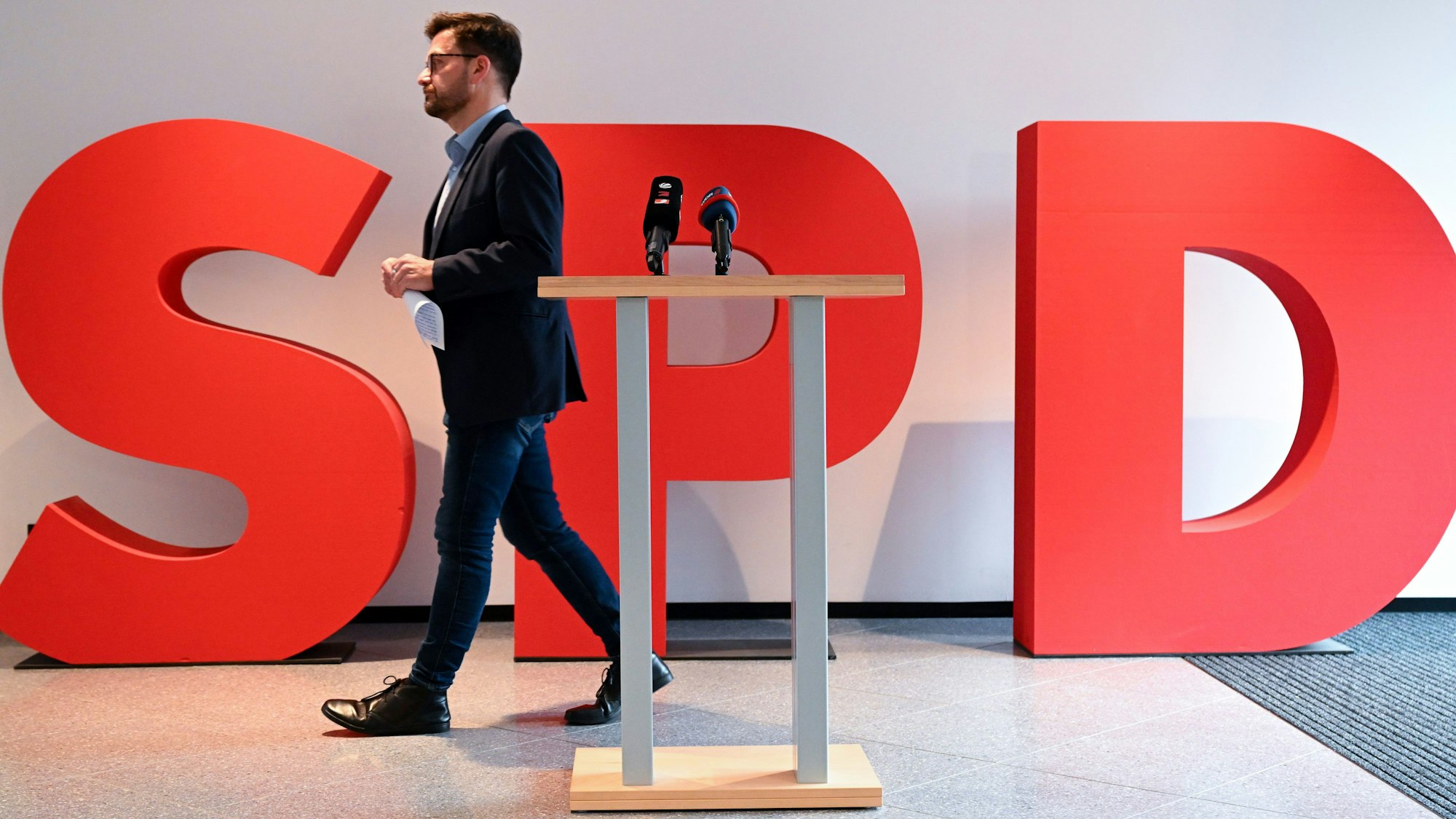 Thomas Kutschaty ist als Landesvorsitzender der SPD in NRW zurückgetreten. Er geht nach einer Rede, im Vodergrund steht ein Rednerpult, im Hintergrund drei große Buchstaben, die SPD bilden.
