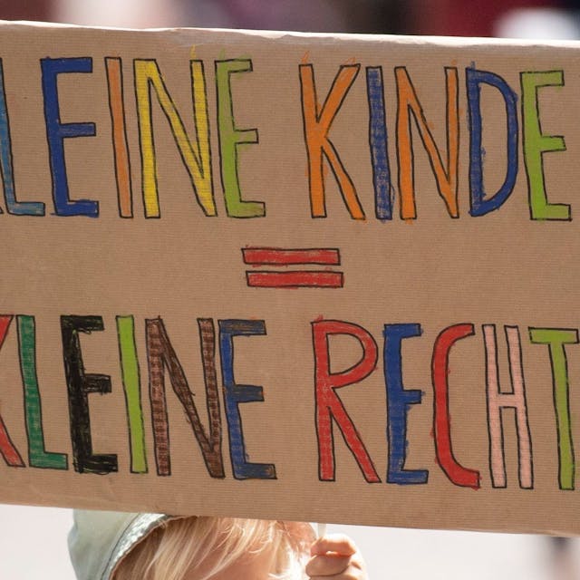 Ein Kind hält ein Plakat mit der Aufschrift „Kleine Kinder, Kleine Rechte?“ bei einem Protest.