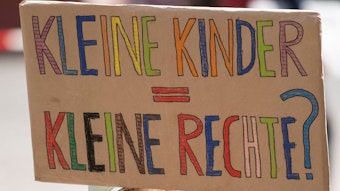 Ein Kind hält ein Plakat mit der Aufschrift „Kleine Kinder, Kleine Rechte?“ bei einem Protest.