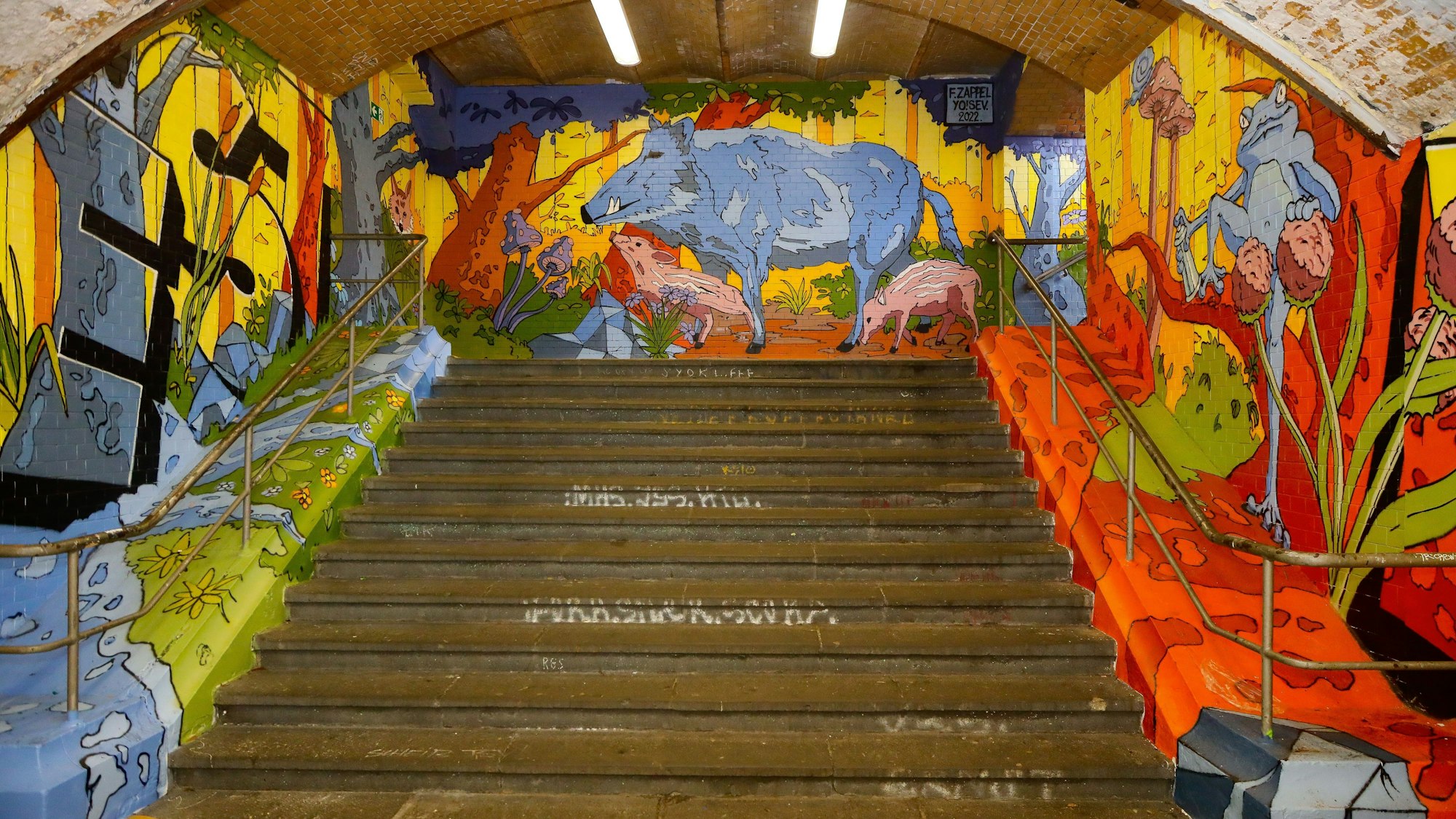 Kunst im Bahnhof Köln-West: Auf drei mit Graffiti beschriebenen Wänden ist eine bunte Waldszene mit Wildschweinen, Rehen und anderen Tieren zu sehen.