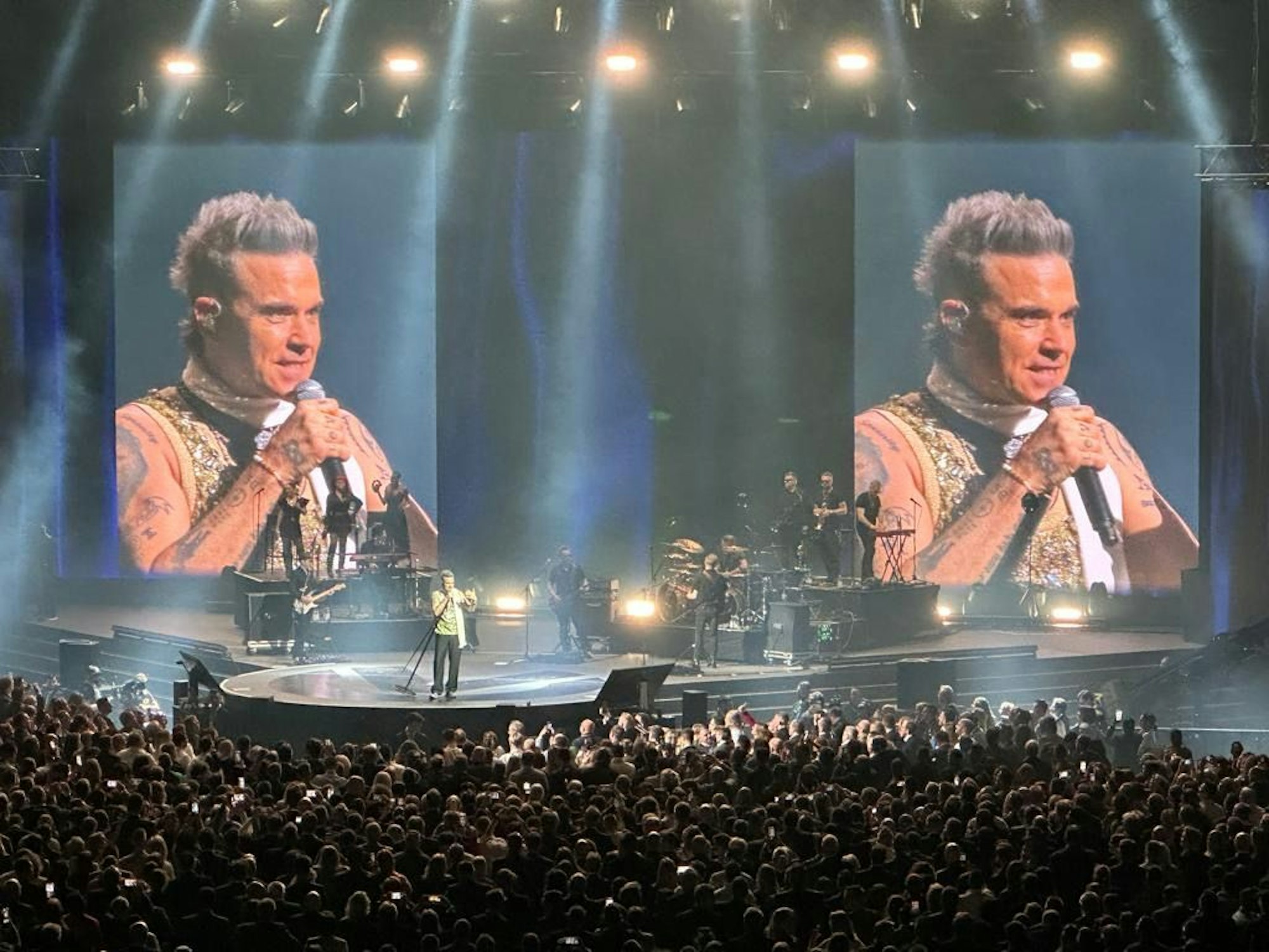 Musiker Robbie Williams steht auf einer Bühne vor Publikum.