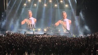 Eine Menschenmenge steht um eine Bühne. Auf großen LED-Wänden sieht man Robbie Williams.