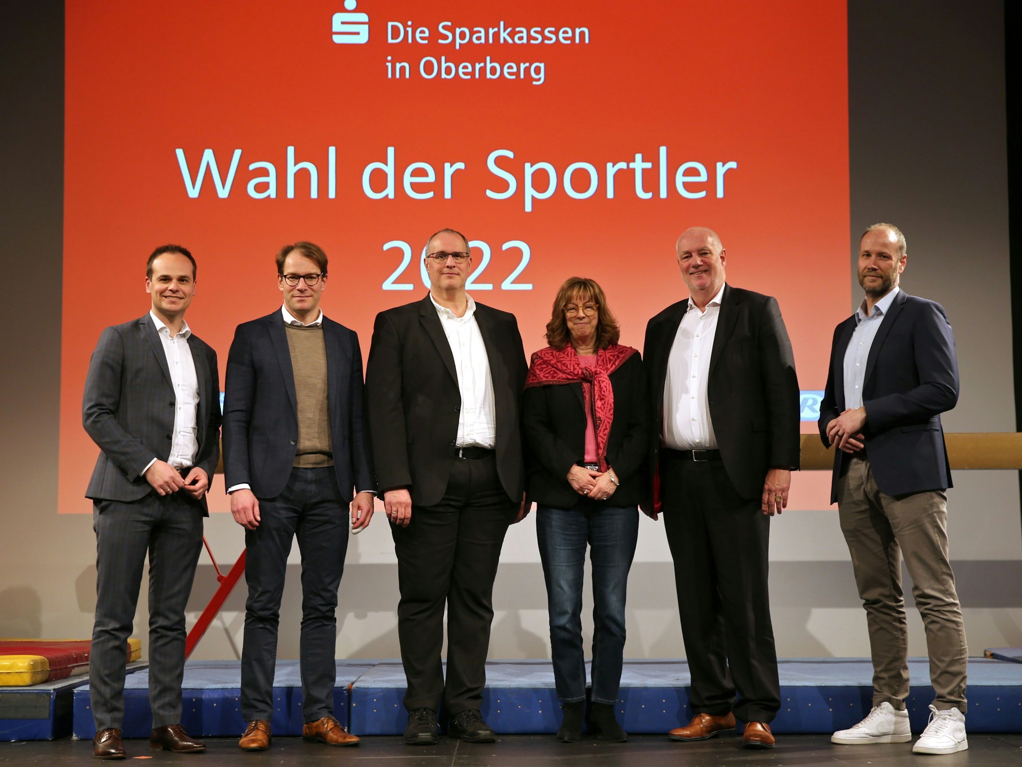 Mehrere schick gekleidete Männer und Frauen stehen nebeneinander auf einer Bühne vor einer Leinwand mit der Aufschrift „Wahl der Sportler 2022“.
