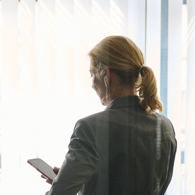 Eine Frau steht in einem Büro und schaut auf ihr Smartphone.
