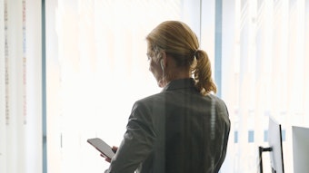 Eine Frau steht in einem Büro und schaut auf ihr Smartphone.