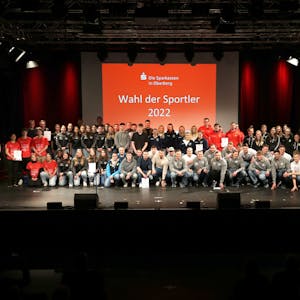 Auf einem Gruppenbild stehen zahlreiche Sportmannschaften vor einer roten Leinwand mit dem Logo der Sparkassen aus Oberberg und der weißen Aufschrift „Wahl der Sportler 2022“.