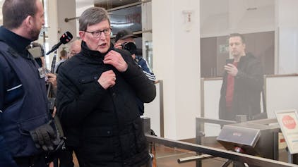 Kardinal Rainer Woelki wird im Foyer des Landgerichts von einem Justizbeamten zur Sicherheitsschleuse begleitet.