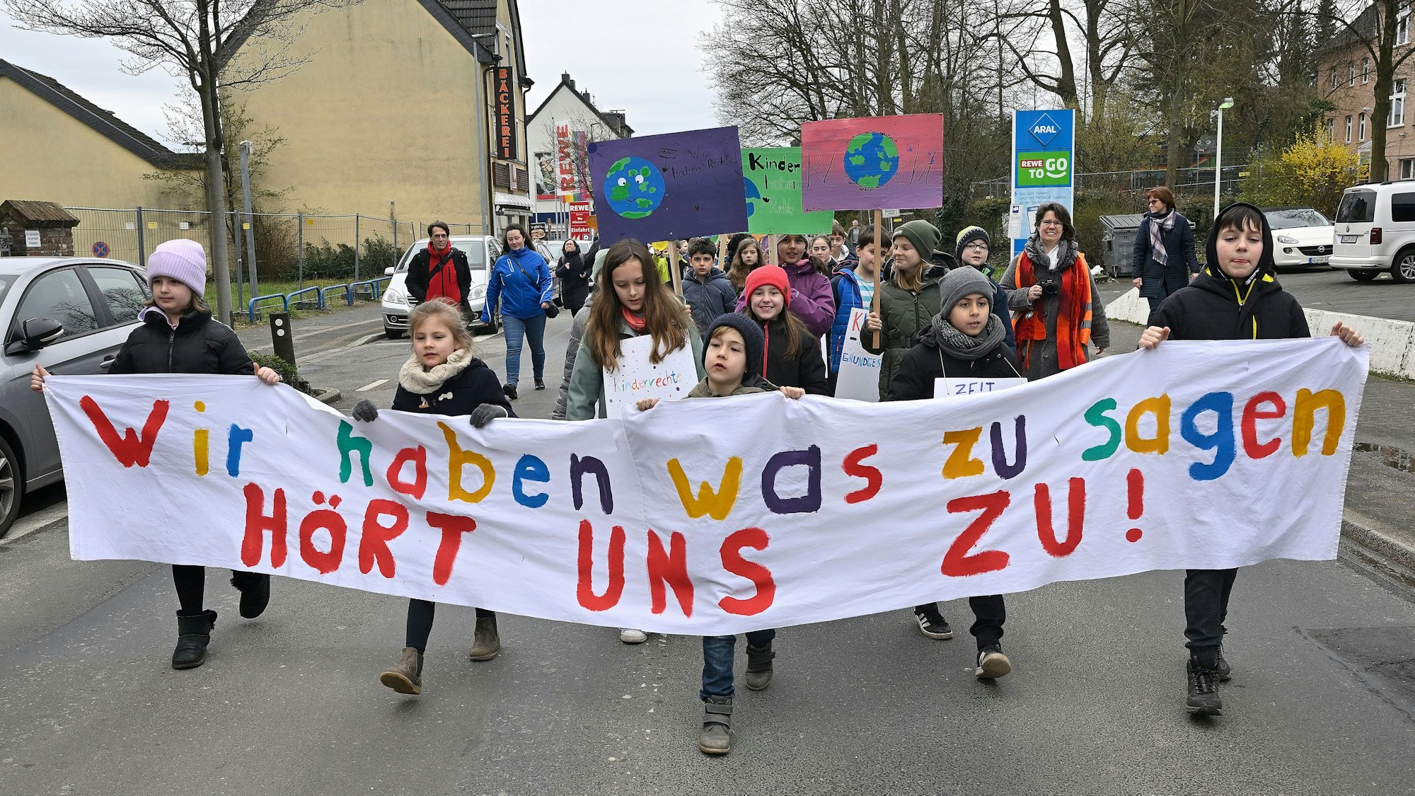 Kinder laufen auf der Straße und halten ein Banner mit der Aufschrift „Wir haben was zu sagen, hört uns zu“.