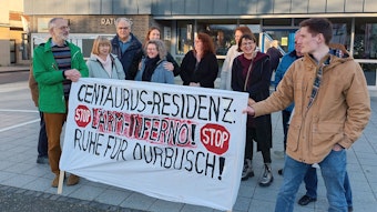 Einige Personen demonstrieren vor dem Rathaus. Sie halten ein Banner, auf dem steht: „Centaurus-Residenz: Lärm-Inferno! Ruhe für Durbusch!“