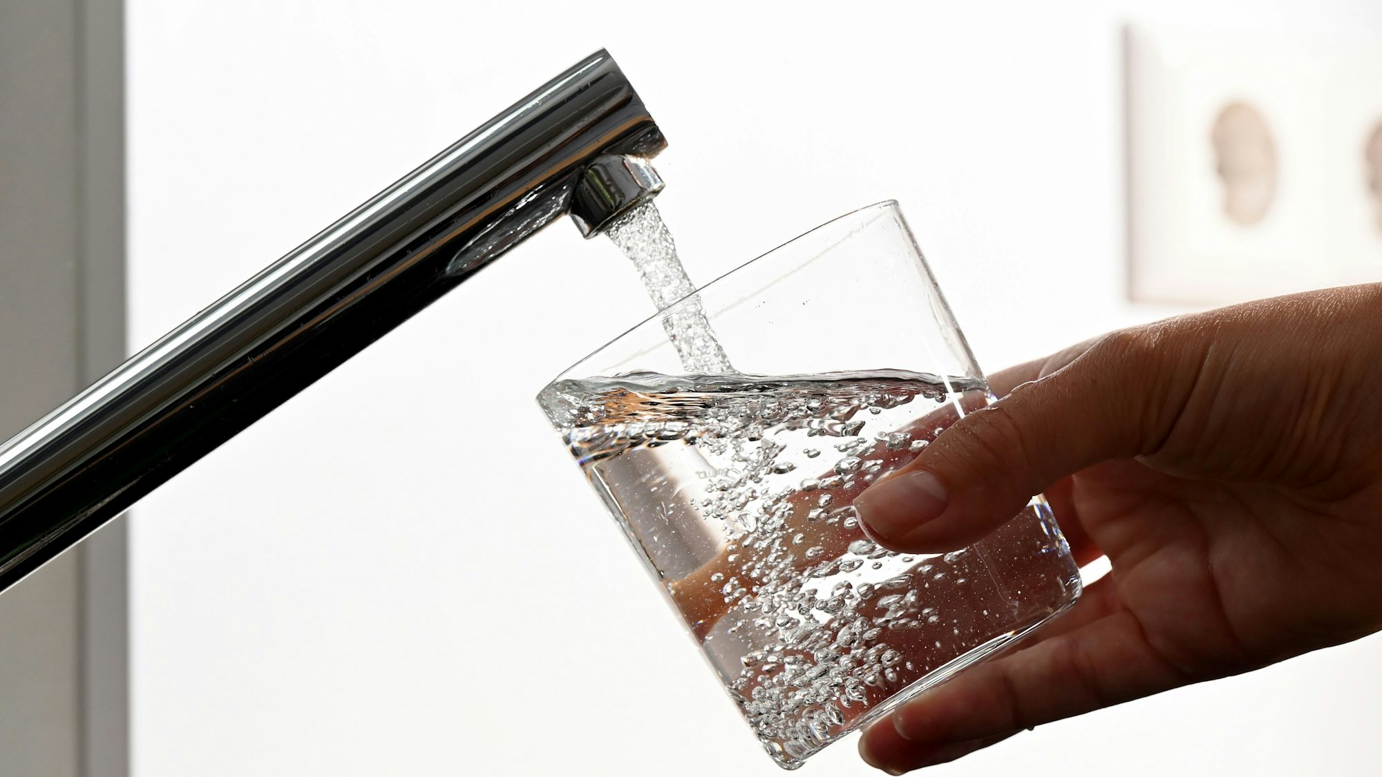 ILLUSTRATION - Eine Hand hält ein Wasserglas unter einen Wasserhahn.