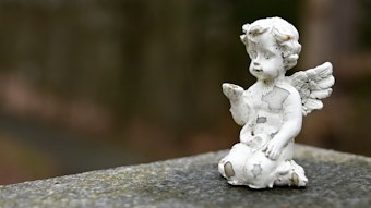 Eine kleine Cherub-Statue aus Porzellan kniet auf einem Grabstein.