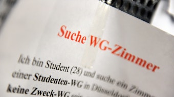 Ein Zettel mit der Aufschrift „Suche WG-Zimmer“ hängt an einem Schwarzen Brett.