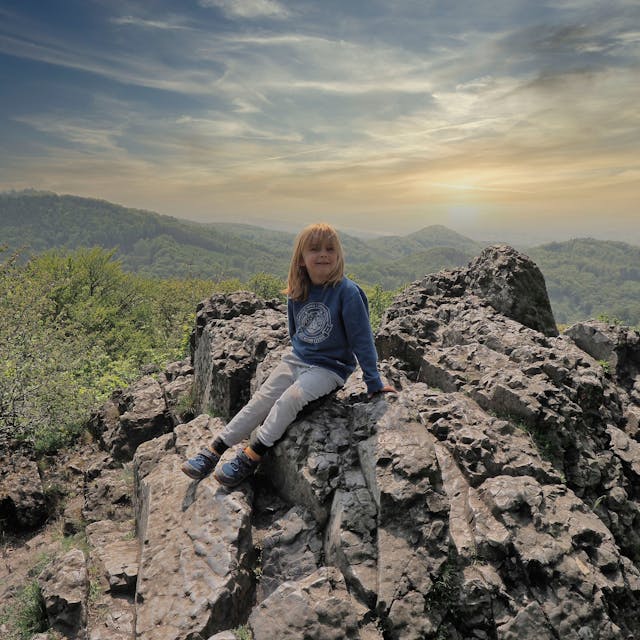 Ein Junge sitzt auf einem Felsen, im Hintergrund ist das Panorama des Siebengebirges zu sehen.