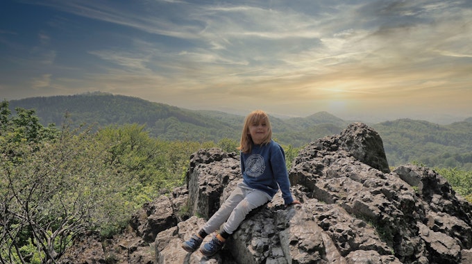 Ein Junge sitzt auf einem Felsen, im Hintergrund ist das Panorama des Siebengebirges zu sehen.