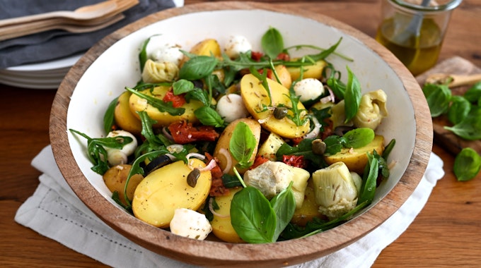 In einer Schüssel sind Kartoffeln, Rucola, Mozzarella, Artischocken, Oliven und getrocknete Tomaten zu einem Salat zubereitet.