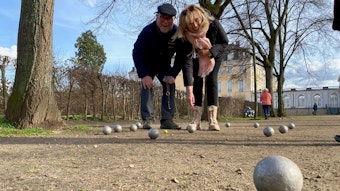 Zwei Menschen spielen Boule in einem Park.