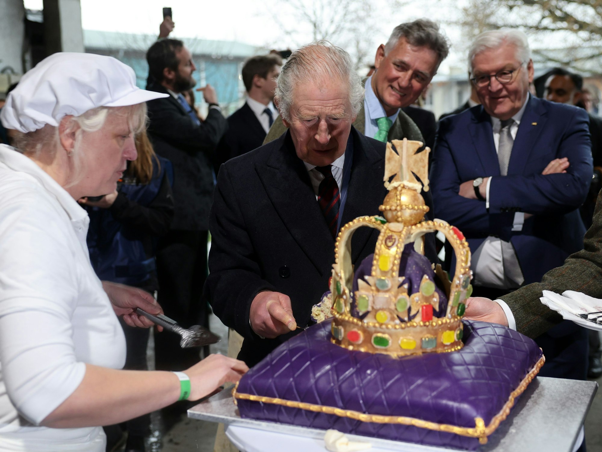 König Charles III. von Großbritannien schneidet im Ökodorf Brodowin eine Torte an, die speziell für seinen Besuch angefertigt wurde. Daneben stehen Bundespräsident Frank-Walter Steinmeier und Ludolf von Maltzan.