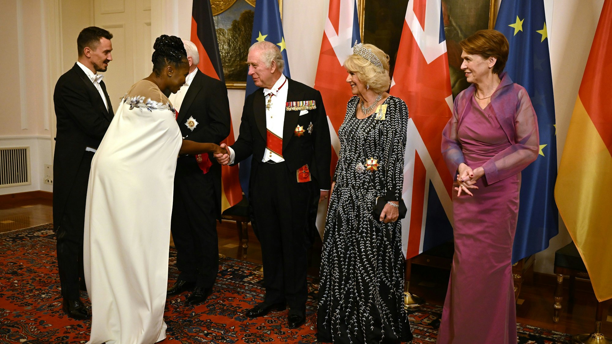 Motsi Mabuse (2.v.l.) schüttelt die Hand von König Charles III. (M.), daneben Königsgemahlin Camilla (2.v.r.) und Elke Büdenbender (r.), die Frau von Bundespräsident Steinmeier.