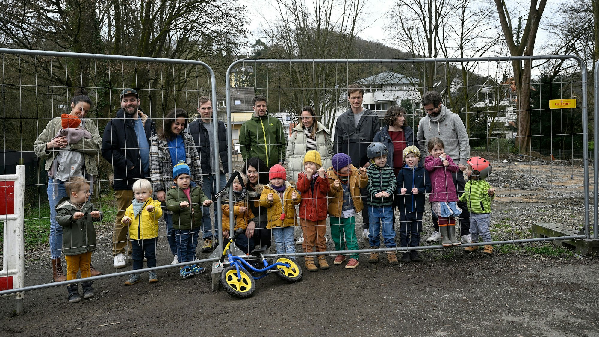Eltern und Kinder stehen hinter einem Bauzaun am noch gesperrten Spielplatz an der Sülz in Rösrath.