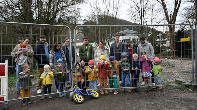 Eltern und Kinder stehen hinter einem Bauzaun am noch gesperrten Spielplatz an der Sülz in Rösrath.
