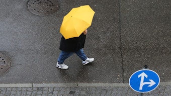 Eine Frau mit Regenschirm in der Hand läuft an einem Verkehrszeichen vorbei