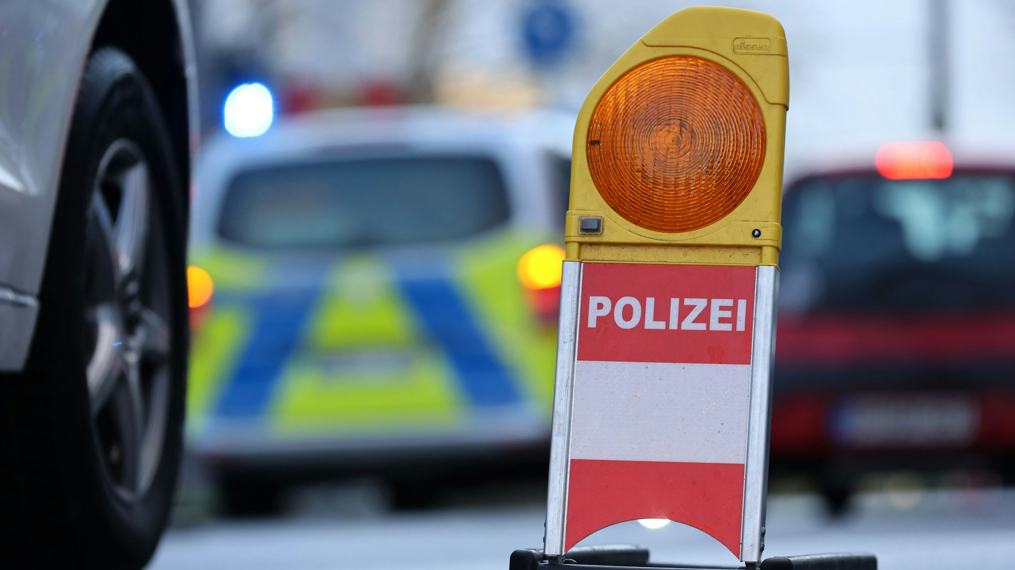 Eine Polizei-Warnbake steht auf einer Kölner Straße. Autos fahren im Hintergrund. (Symbolbild)