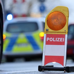 Eine Polizei-Warnbake steht auf einer Kölner Straße. Autos fahren im Hintergrund. (Symbolbild)