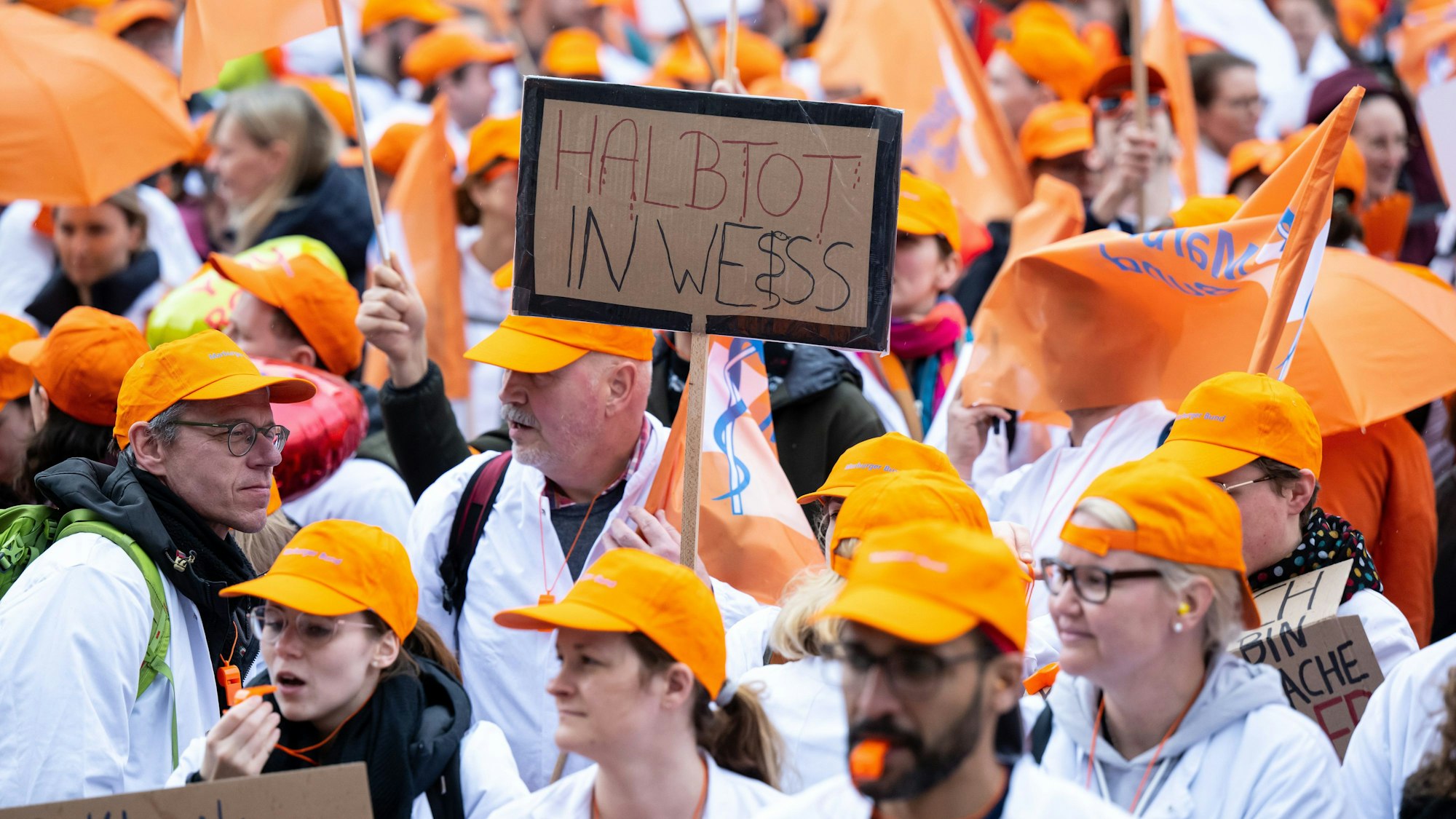 Teilnehmerinnen und Teilnehmer eines Warnstreiks der Gewerkschaft Marburger Bund nehmen an einer Demonstration teil und halten ein Plakat mit der Aufschrift „Halbtot in weiß“ in den Händen.