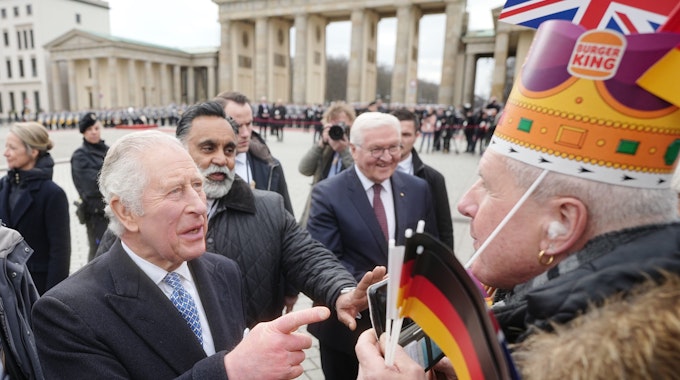 König Charles III. von Großbritannien am Brandenburger Tor mit Bundespräsident Frank-Walter Steinmeier. Ihm gegenüber steht ein Mann mit einer Krone der Fast-Food-Kette „Burger King“.
