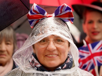 Ein Royal-Fan trägt eine Schleife in den Farben der britischen Nationalflagge auf der Kapuze ihres Regenmantels und wartet bei Regen am Rathausmarkt vor dem Hamburger Rathaus auf die Ankunft des britischen Königspaares.