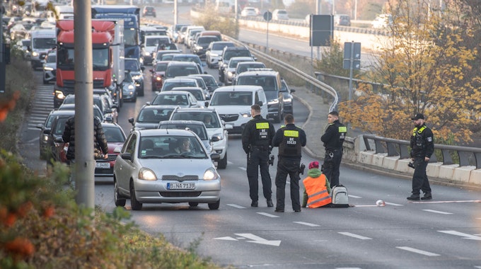 Eine Demonstrantin der Gruppe "Letzte Generation" sitzt, umringt von Polizeibeamten, auf der Ausfahrt der Stadtautobahn am Sachsenring.