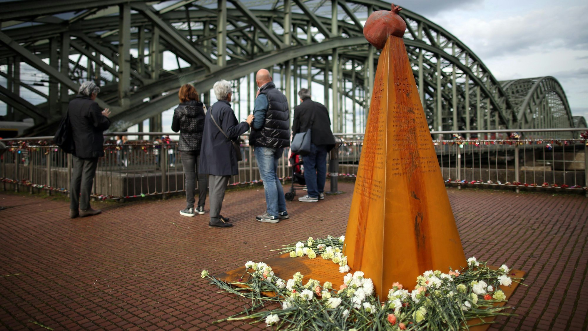 Das Mahnmal, finanziert vom Verein „Völkermord erinnern“, stand bereits am Heinrich-Böll-Platz nahe der Hohenzollernbrücke. Eine etwa drei Meter hohe Pyramide mit Inschriften ist umgeben von Blumen.