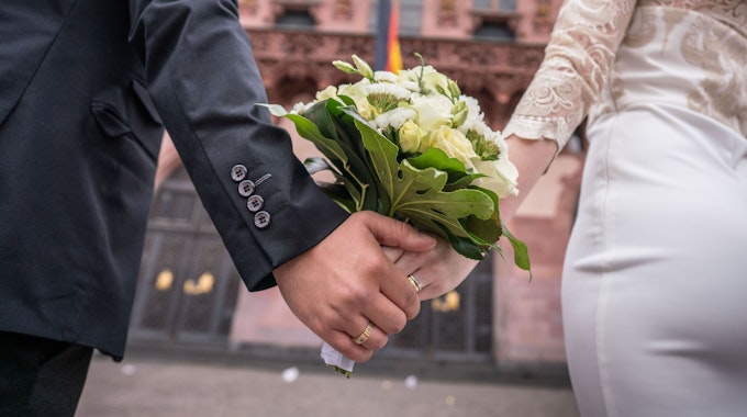 Ein Brautpaar steht nach der Trauung Hand in Hand für ein Foto bereit.