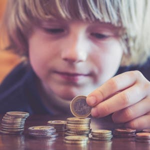Ein kleiner Junge mit längeren blonden Haaren türmt Münzgeld aufeinander.