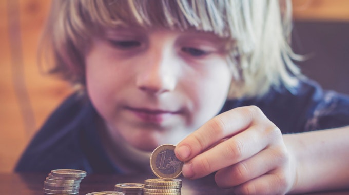 Ein kleiner Junge mit längeren blonden Haaren türmt Münzgeld aufeinander.