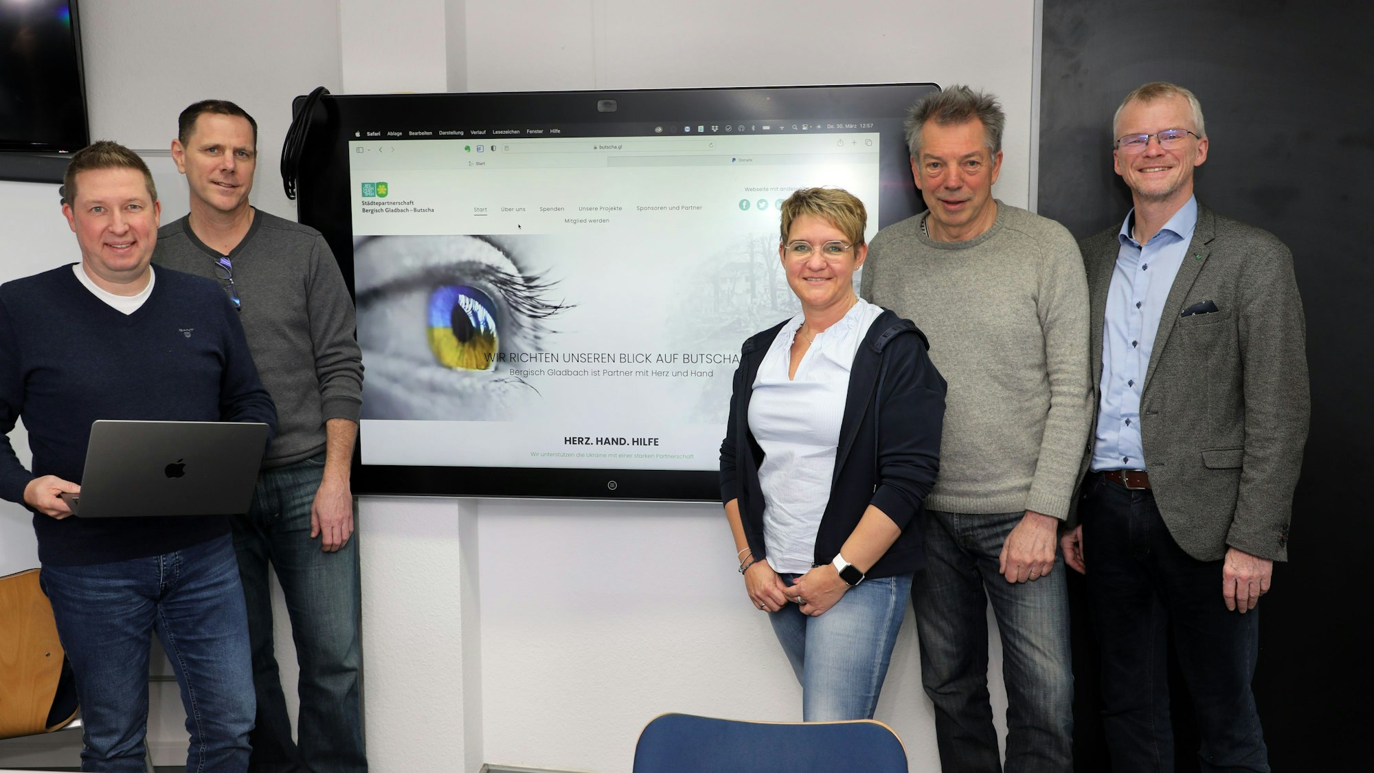Vier Männer und eine Frau stehen vor der Ansicht einer Webseite des Vereins zur Förderung der Städtepartnerschaft Butscha - Bergisch Gladbach.