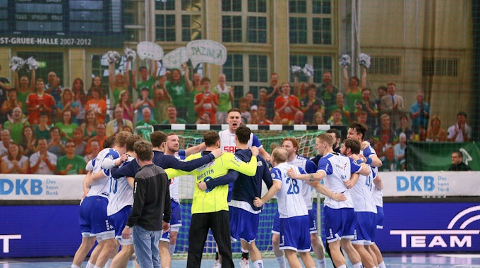 Eine Handballmannschaft steht im Kreis zusammen, die Spieler liegen sich in den Armen und feiert hüpfend den Sieg.