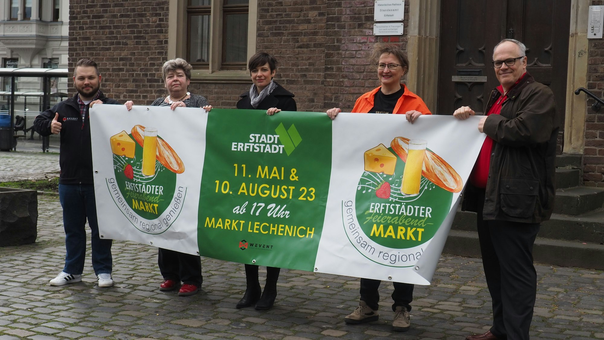 Die zwei Männer und drei Frauen halten das grün-weiße Banner mit dem Logo des geplanten Feierabendmarktes in den Händen.