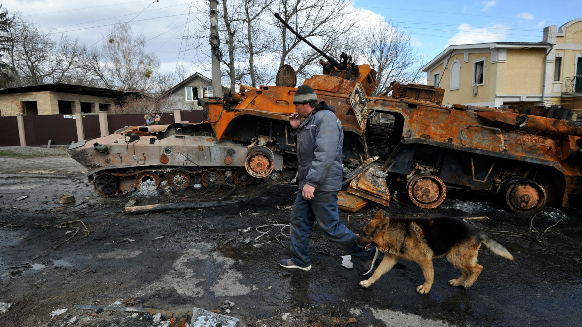 Ein Mann geht mit seinem Hund an zerstörten Militärfahrzeugen der russischen Armee vorbei. Angesichts der schockierenden Gräueltaten in der ukrainischen Stadt Butscha bereitet der Westen schärfere Sanktionen gegen Russland vor. +++ dpa-Bildfunk +++