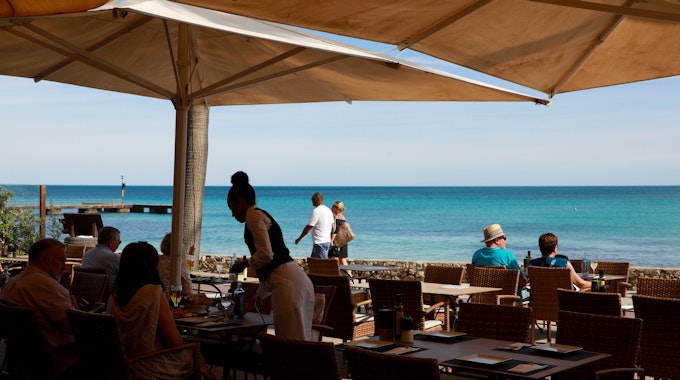 Eine Kellnerin des Restaurants Sa Caleta, serviert den Gästen am Strand von Cala Millor auf Mallorca etwas. 