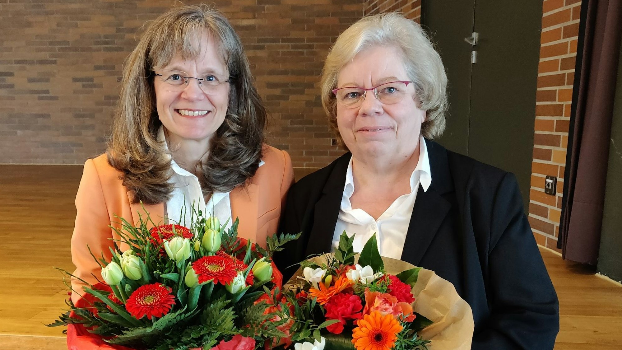 Ulrike Detering und Helga Lagotzky stehen mit Blumensträußen vor der Bühne im Haus der Kunst.