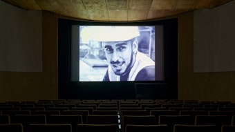 Installationsansicht aus dem Kino des Kölnischen Kunstvereins mit einem Bauarbeiter, der in die Kamera schaut.