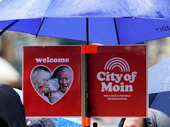Royal-Fans haben an einen Regenschirm ein Plakat mit der Aufschrift „Welcome - City of Moin“ befestigt und warten am Rathausmarkt vor dem Hamburger Rathaus auf die Ankunft des britischen Königspaares.