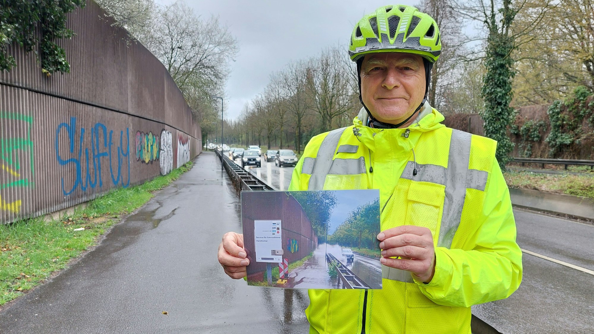 ADFC-Vorsitzender Kurt Krefft hält auf einem Radweg ein Foto derselben Stelle mit Baustelle in der Hand.