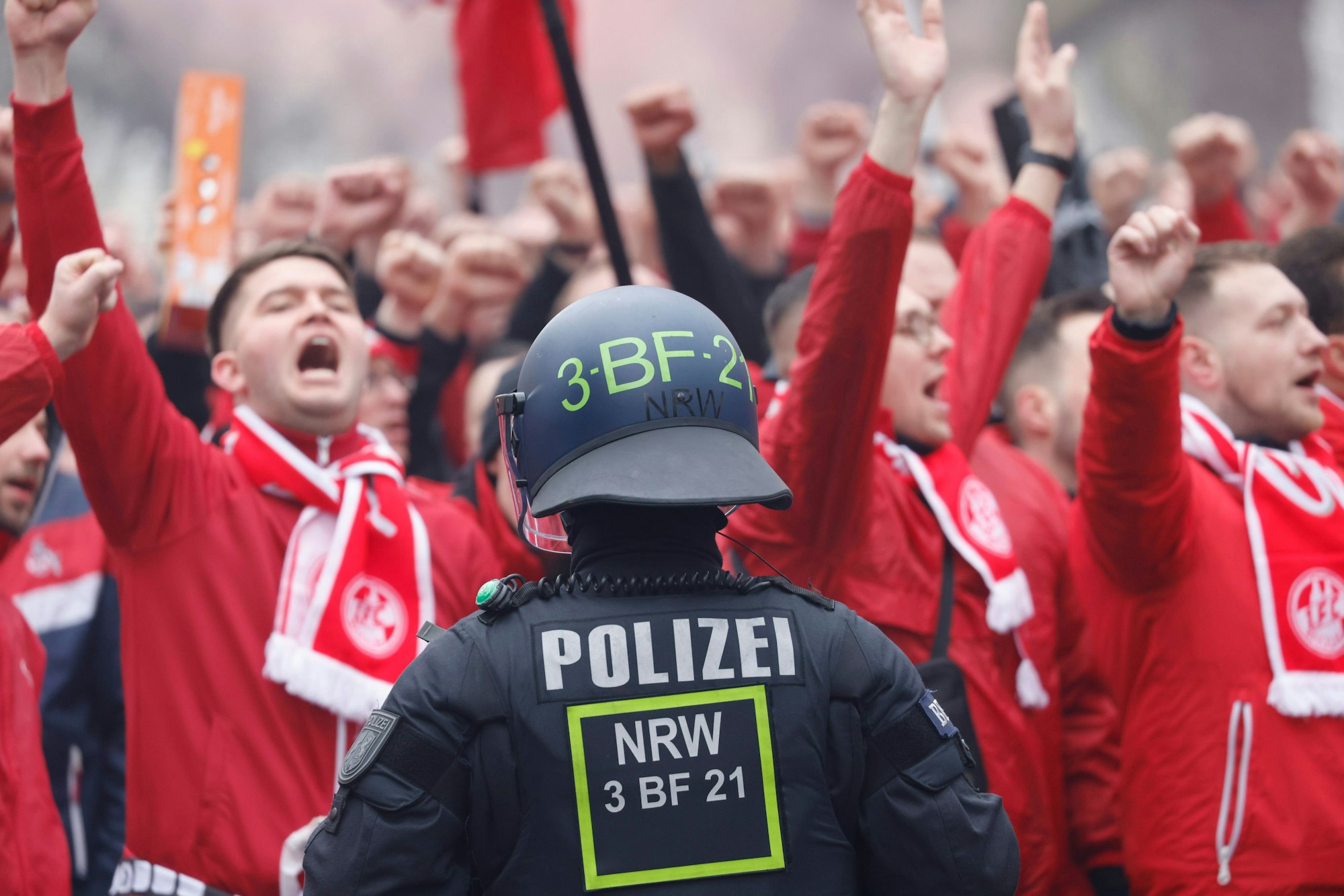 Skandierende Fans des 1. FC Köln stehen vor dem Stadion einem Polizisten gegenüber.