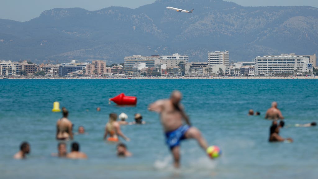 Ein Flugzeug fliegt über das Meer, während Urlauber im Wasser baden.