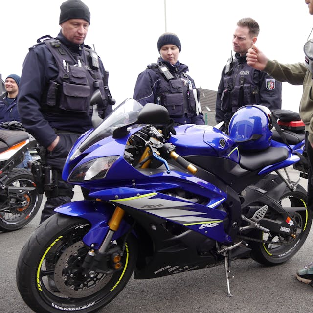 Eine Polizeibeamtin und zwei Polizeibeamte schauen auf ein blaues Motorrad.