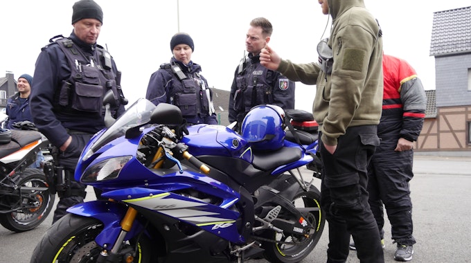 Eine Polizeibeamtin und zwei Polizeibeamte schauen auf ein blaues Motorrad.