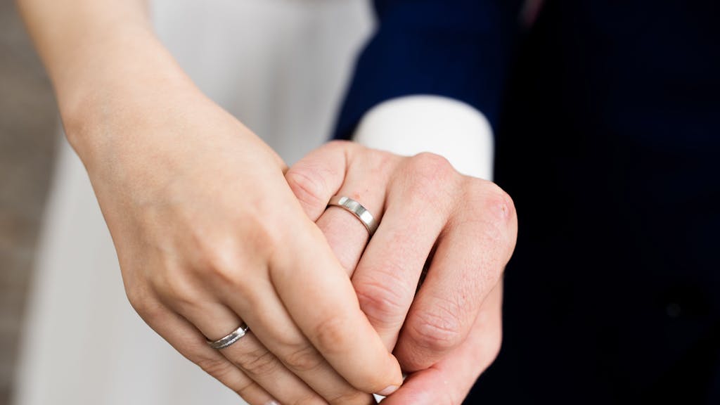 Eine Frauen- und eine Männerhand mit silbernen Eheringen.