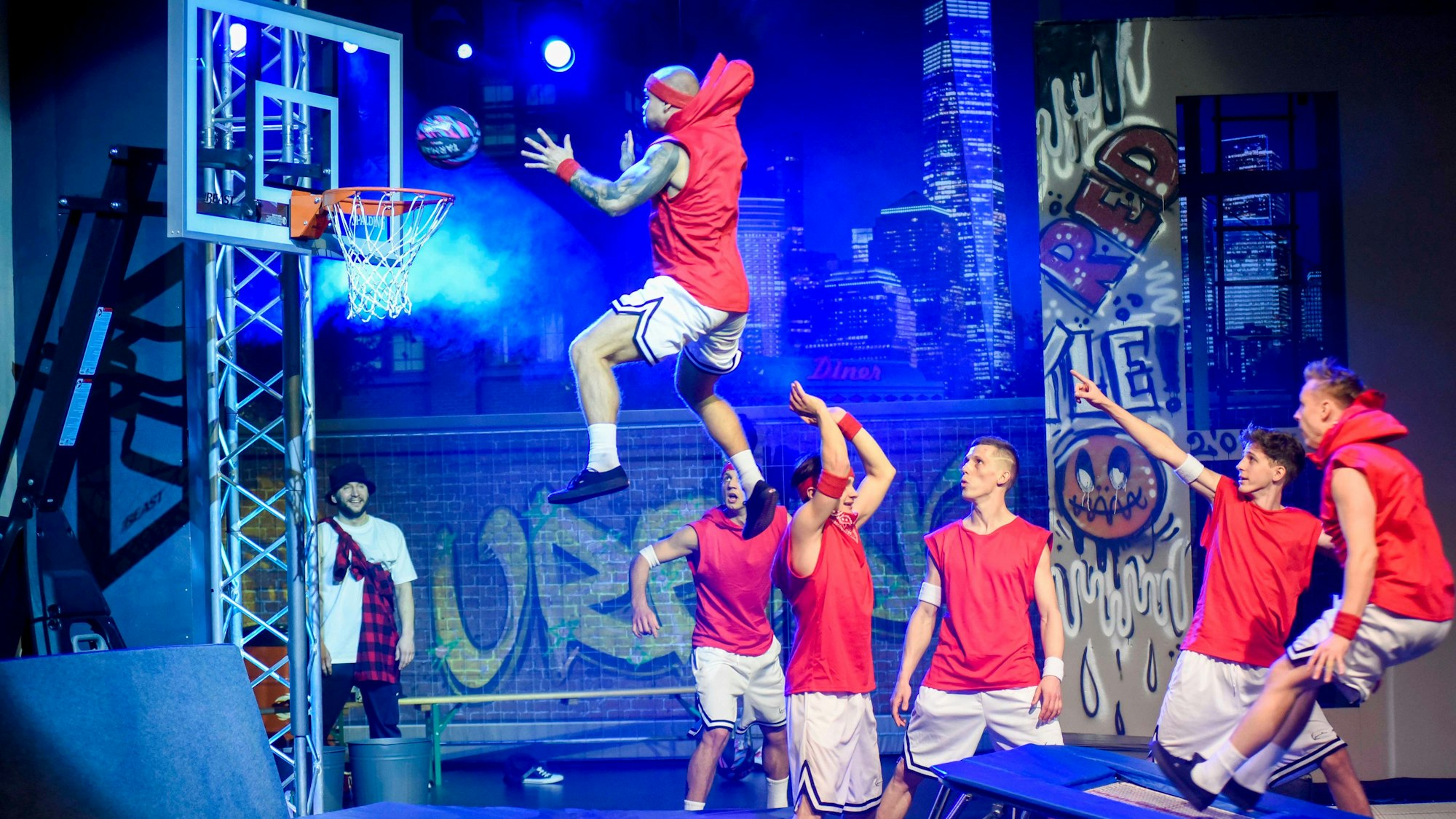 Das Bild zeigt sechs junge Männer, die akrobatisch von einem Trampolin an einen Basketballkorb springen.